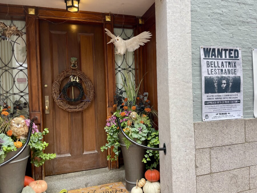 A front door with a pumpkin arrangement and bird in the top right corner along with Wanted posters from Harry Potter.